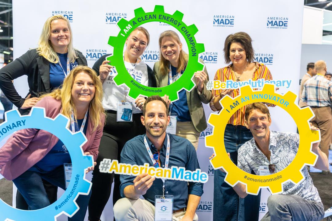 A group of people smiling and holding colorful handheld gears and signs that say “American-Made