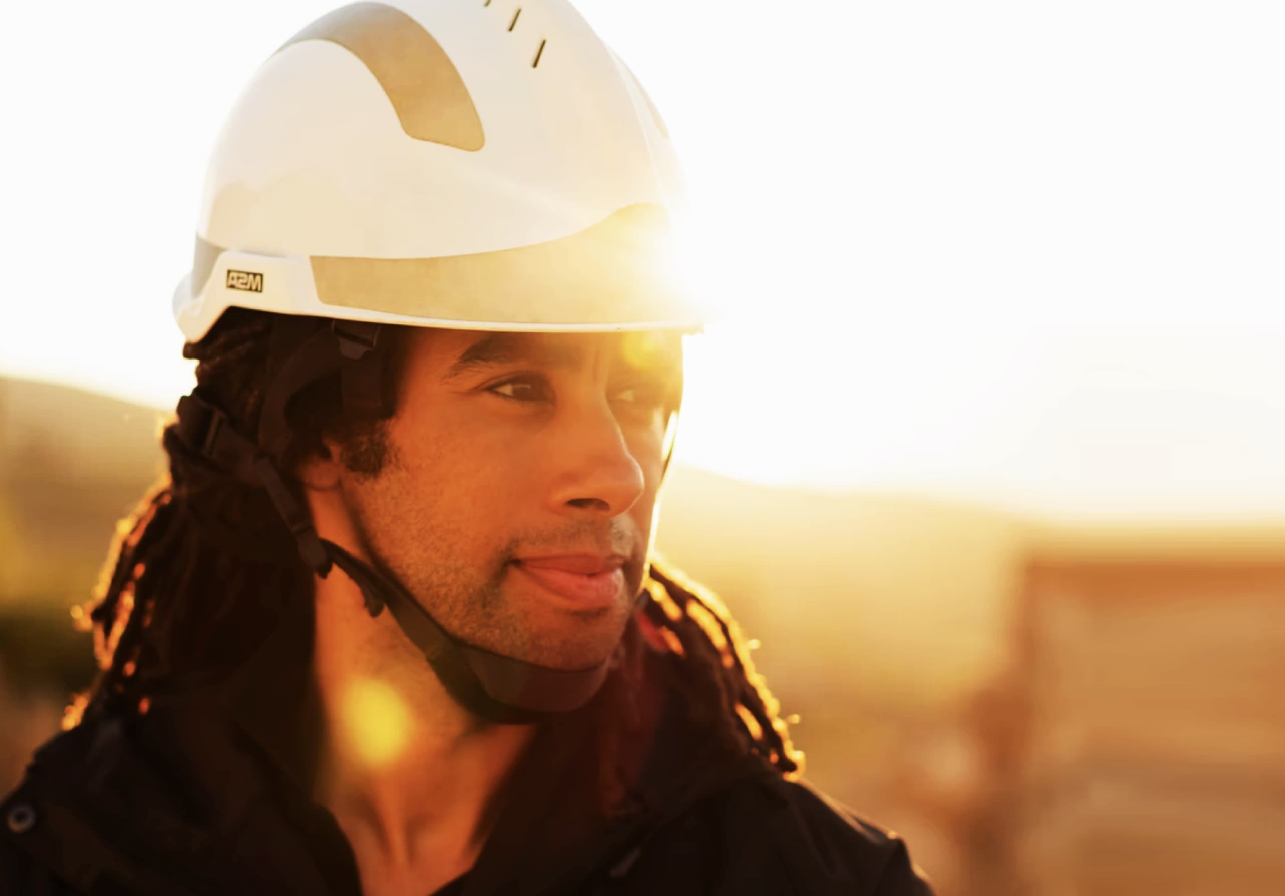 Close up headshot photograph of worker in a hardhat with sunset in background