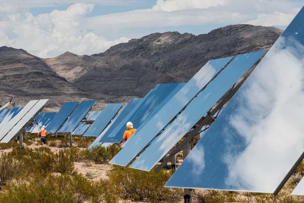 workers and solar panels with mountains in the background.