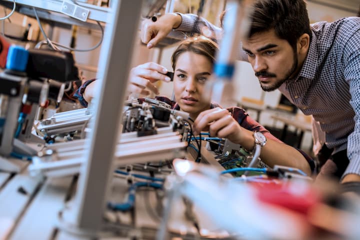 A female researcher works on hardware in a laboratory while a male researcher observes.